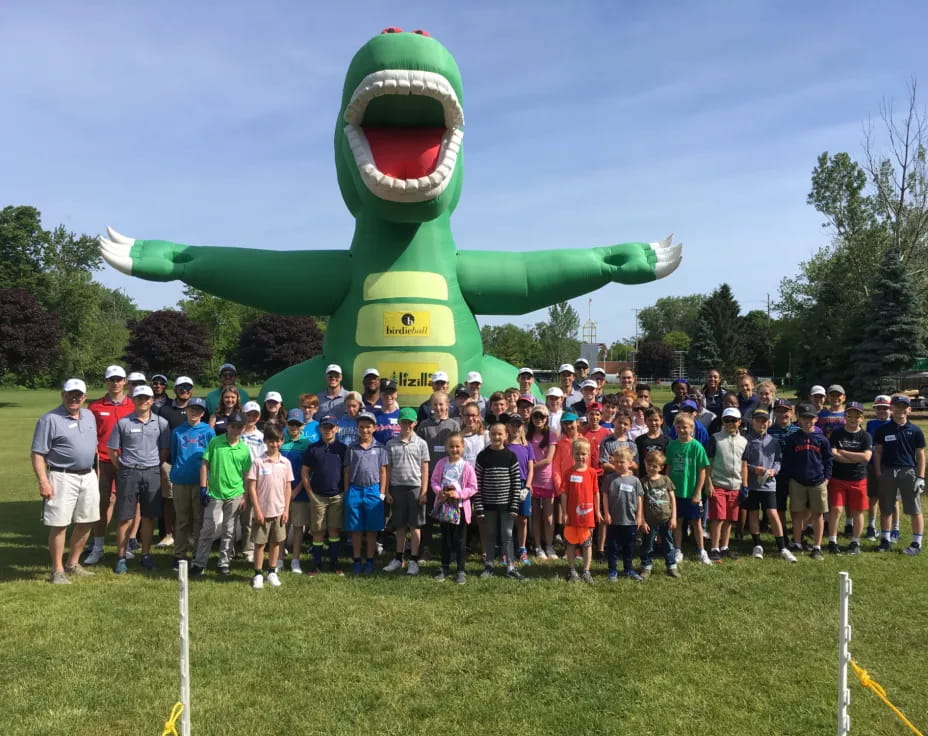 a group of people posing for a photo in front of a large green dinosaur