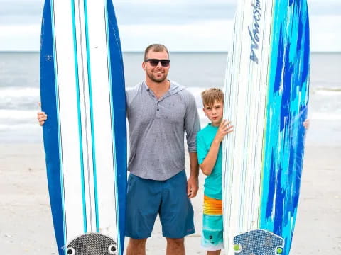 a person and a boy standing next to surfboards on a beach