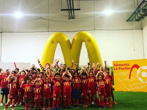 a group of children in red uniforms standing in front of a large yellow mascot