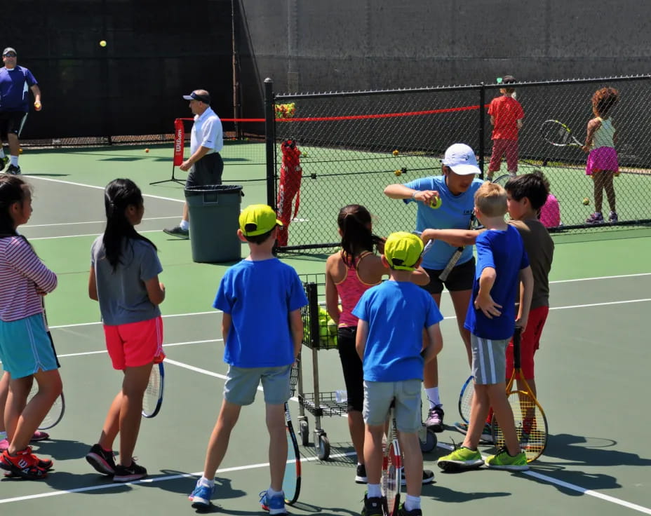 a group of kids stand on a tennis court