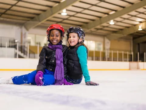 a couple of girls wearing helmets and sitting on ice