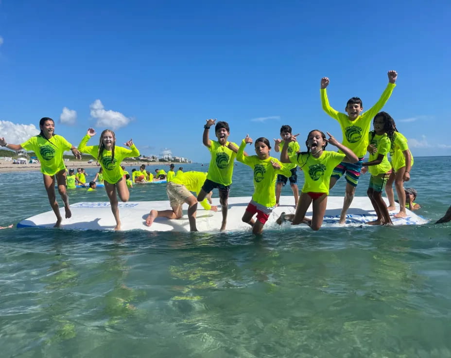 a group of people in green shirts jumping on a surfboard in the water