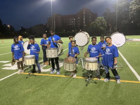 a group of people wearing blue shirts and holding drums on a grass field