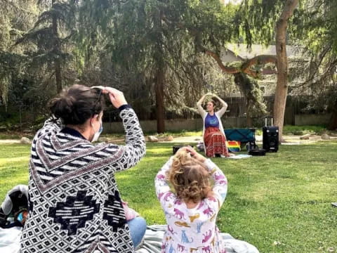 a person and a child sitting on a blanket in a park