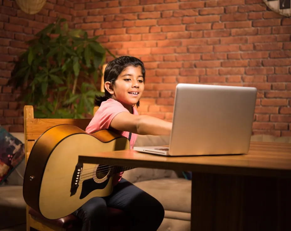 a person sitting at a desk with a laptop and a guitar