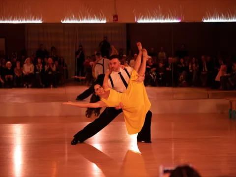 a man and woman dancing on a wood floor with a crowd watching
