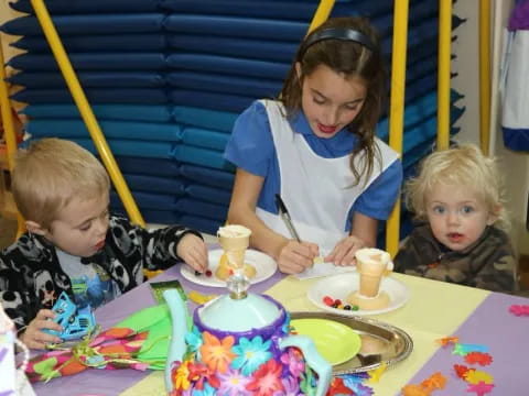 a person and two children sitting at a table with a cake