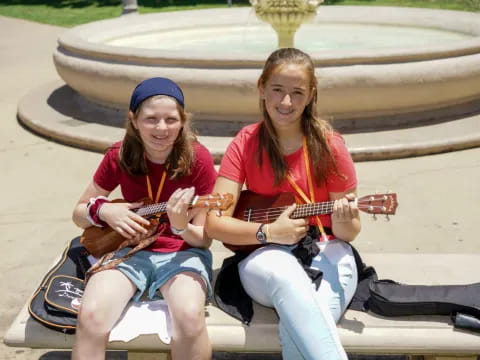 a couple of women sitting on a bench playing guitars