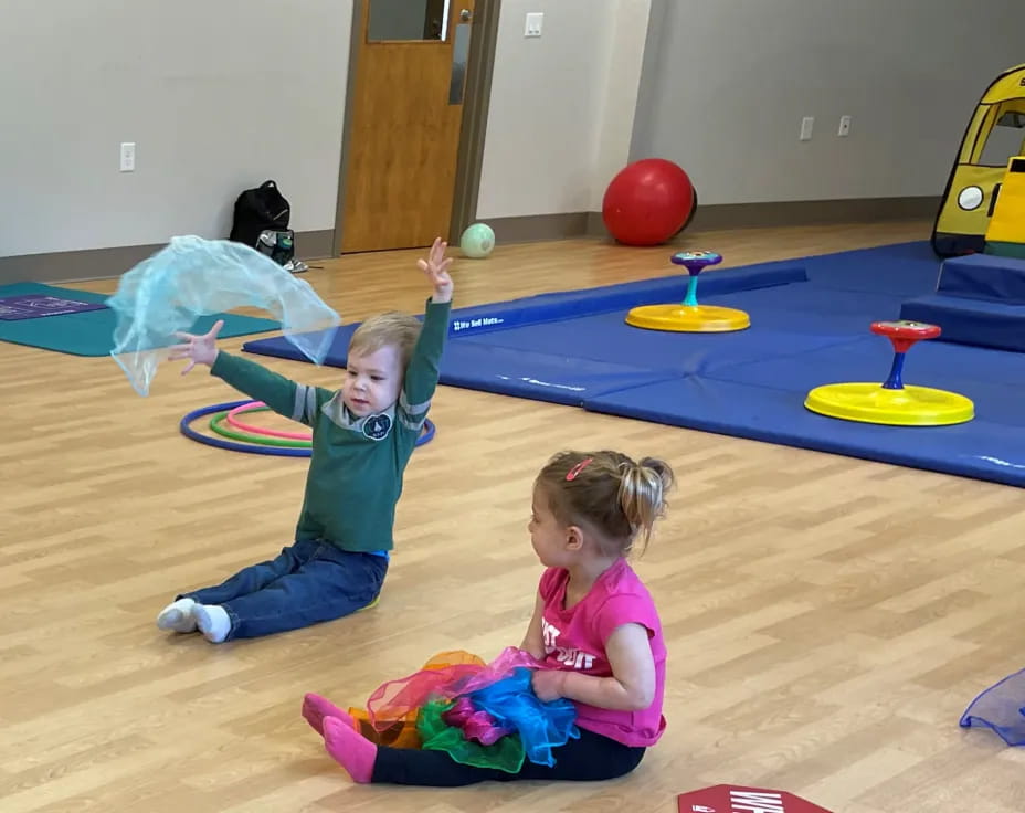 a couple of children playing on a blue mat in a room with a blue table and yellow balls