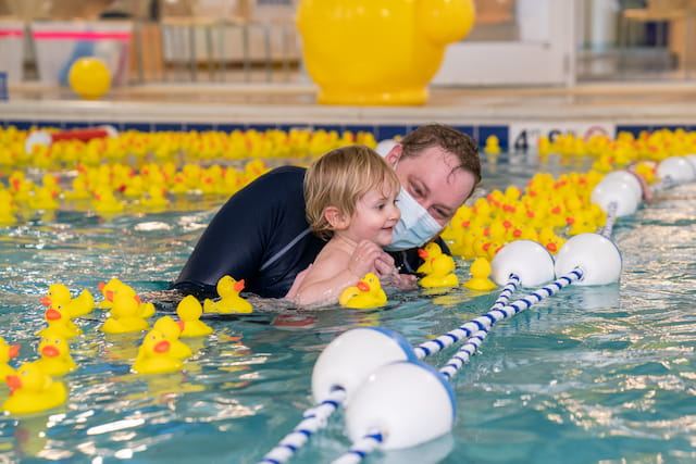 a person and a child in a pool with rubber ducks