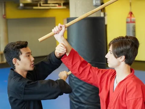 a person holding a wooden stick to another man's head