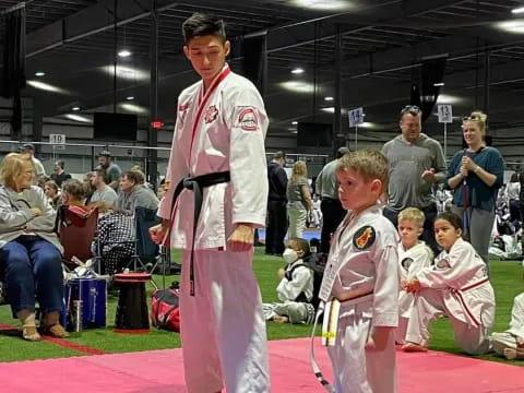 a person and a boy in karate uniforms standing on a mat in front of a crowd of people