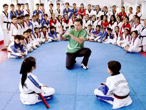 a person kneeling in front of a group of children in karate uniforms