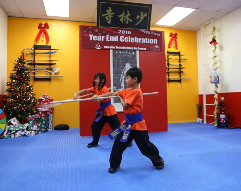 a couple of kids playing with a sword in a room with a christmas tree