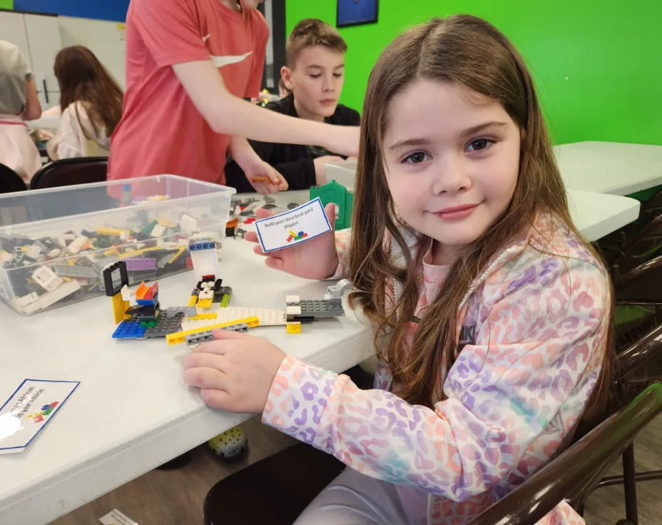 a girl sitting at a table with a toy