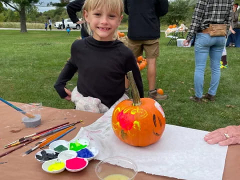 a boy sitting at a table with a pumpkin and other people in the background