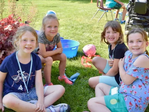 a group of girls sitting on the grass holding a bucket of candy