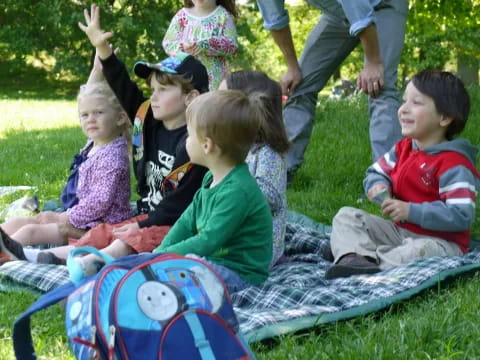 a group of children sitting on a blanket in the grass