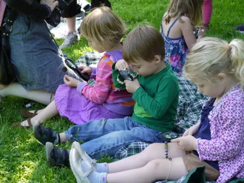 a group of children sitting on the grass looking at a cell phone