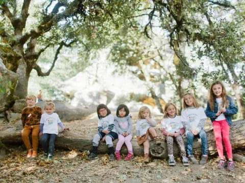 a group of children sitting on a log under a tree