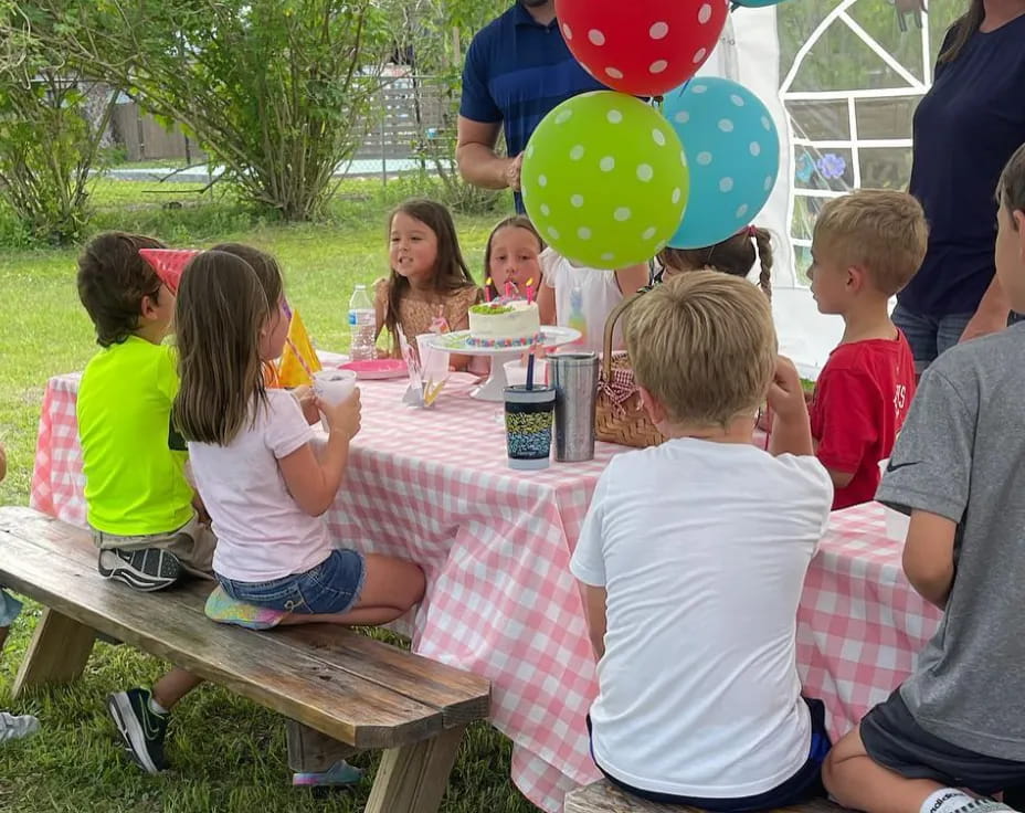 a group of children sitting at a table with food and balloons