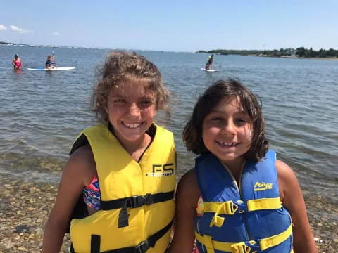two girls wearing life jackets and standing in front of water
