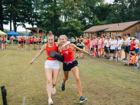 a couple of women running on a grass field with a crowd watching