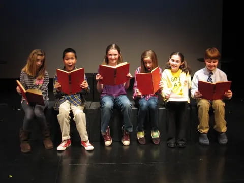 a group of children sitting on a stage holding books