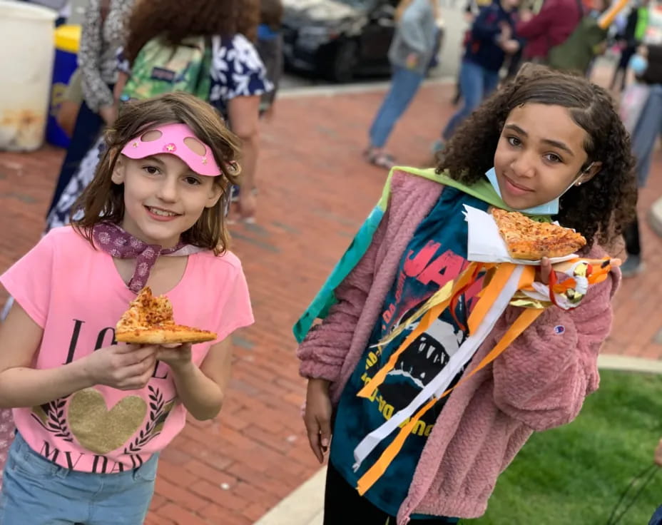 girls eating pizzas on the sidewalk