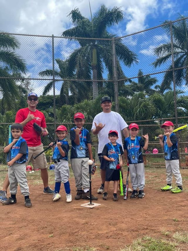 a group of kids posing for a photo in front of a batting cage