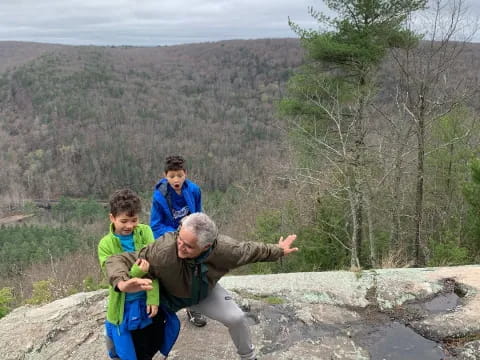 a person and two boys on a rock with trees and hills in the background