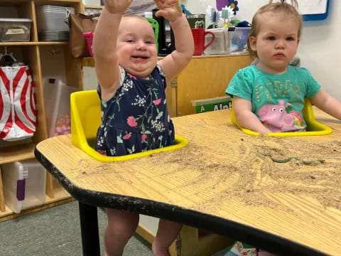 a couple of children sitting at a table with their hands up