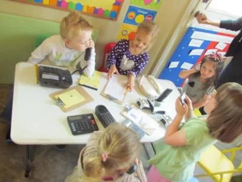 a group of children sitting at a table with computers