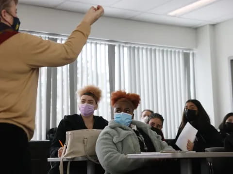 a person in a mask and a mask standing in front of a group of people in a room