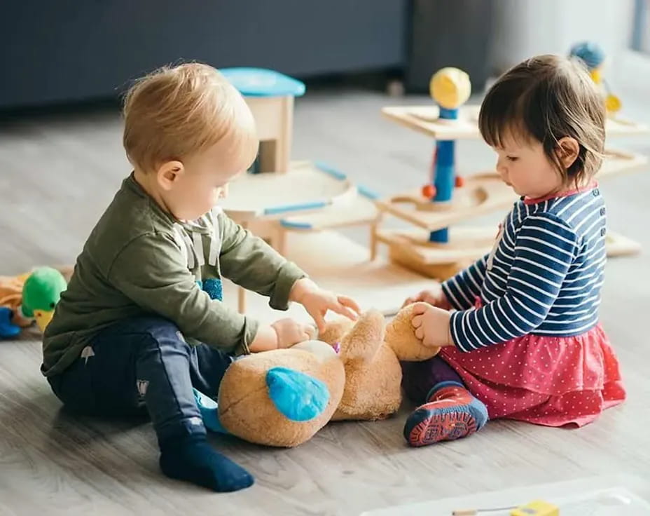 a couple of kids playing with a teddy bear