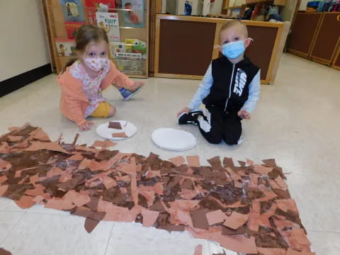 a couple of kids sitting on the floor with food on the floor