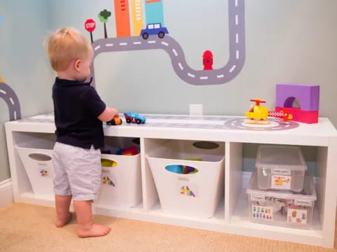 a child standing in front of a white shelf with toys on it