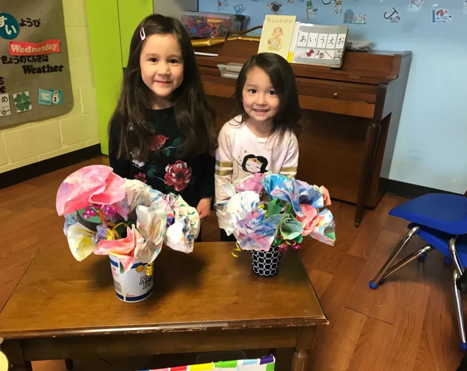 a couple of girls sitting at a table with a basket of easter eggs