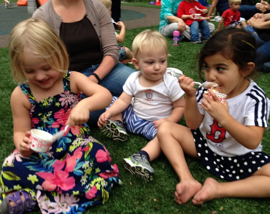 a group of children sitting on the grass eating ice cream