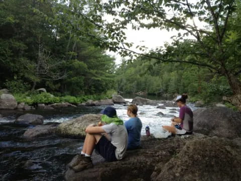 a group of people sitting on rocks by a river