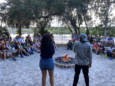 a man and woman standing in front of a fire pit with people sitting around