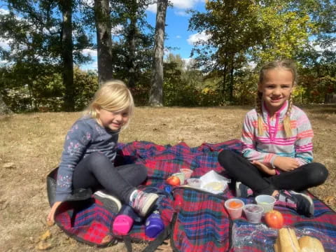 two girls sitting on a blanket outside