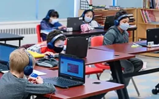 a group of children sitting at desks with laptops