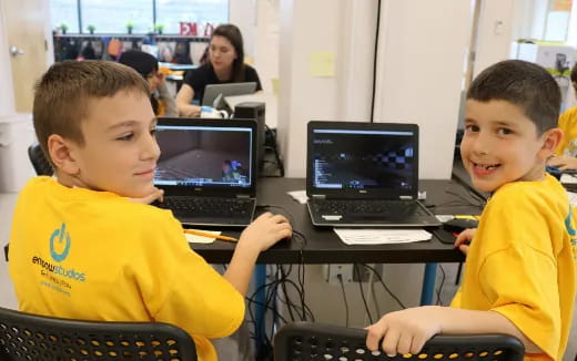 a couple of boys sitting at a desk with laptops