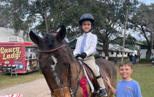 a boy riding a horse with a girl standing next to it