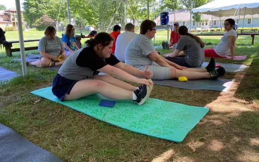 a group of people sitting on a mat in a grassy area