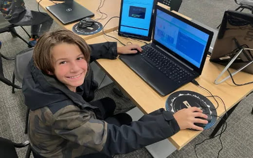 a boy sitting at a desk with a laptop and headphones