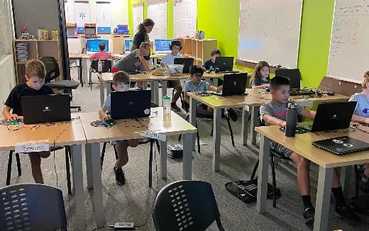 a group of children sitting at desks with laptops