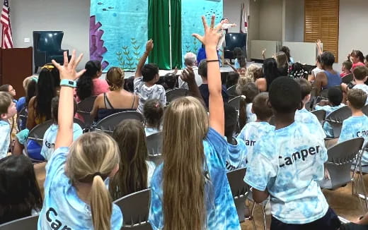 a group of people sitting in a room with their hands up