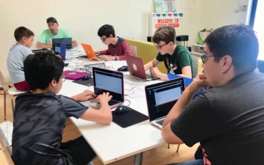 a group of people sitting at a table with laptops